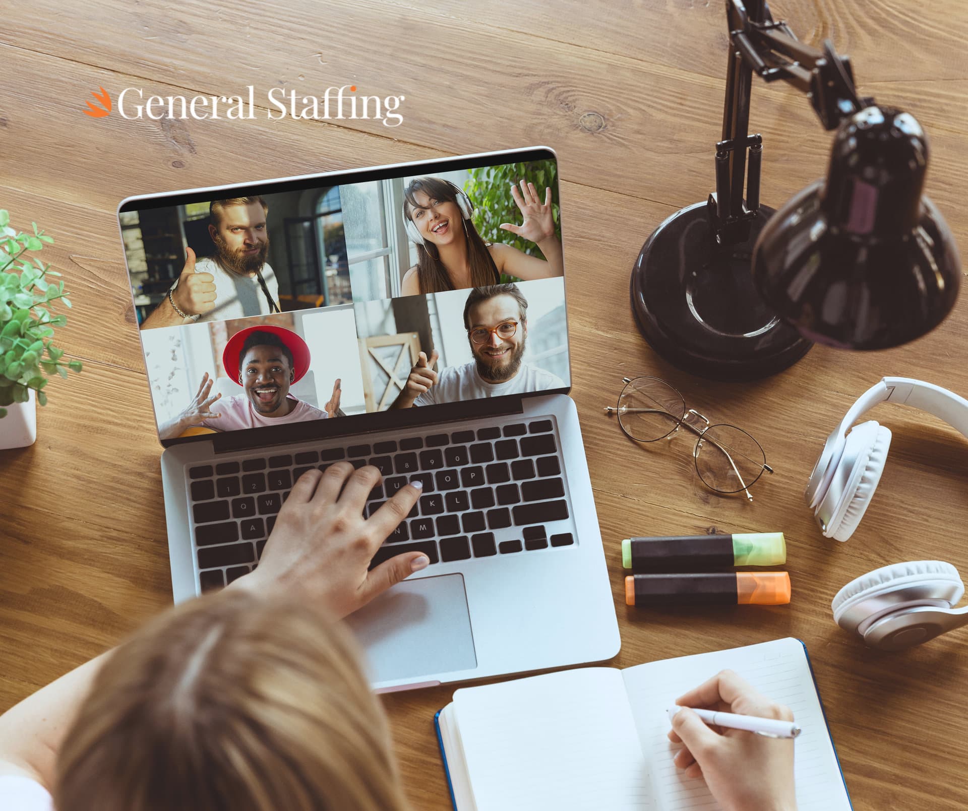 A laptop on a wooden desk showing a video call with four smiling remote workers